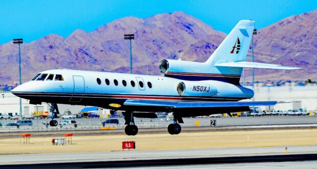 A Dassault Falcon 50 jet is captured landing with mountains in the background, HD Desktop Wallpaper