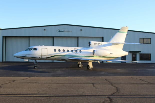 A Dassault Falcon 50 is parked on a tarmac in front of a hangar during daylight, 2K Desktop Wallpaper