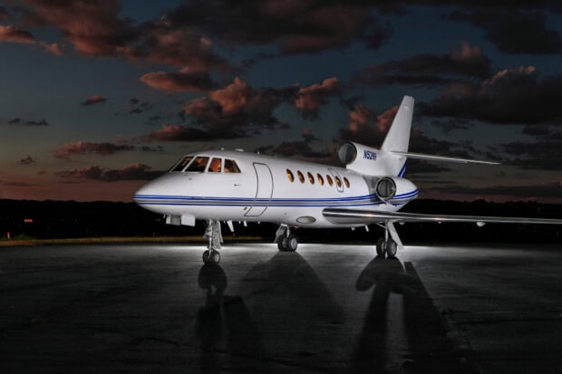 A Dassault Falcon 50 stands on the tarmac under a dark cloudy sky at dusk, 2K Desktop Wallpaper