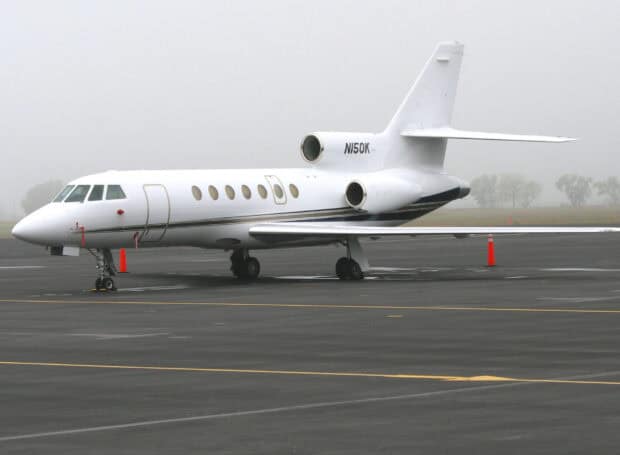 A white Dassault Falcon 50 aircraft is parked on the runway on a foggy day, HD Desktop Wallpaper