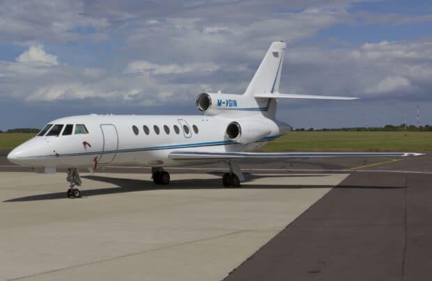 A Dassault Falcon 50 aircraft is parked on an airport runway under a cloudy sky, HD Desktop Wallpaper