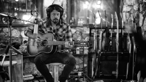Dave Grohl playing an acoustic guitar in a recording studio surrounded by equipment, HD Desktop Wallpaper