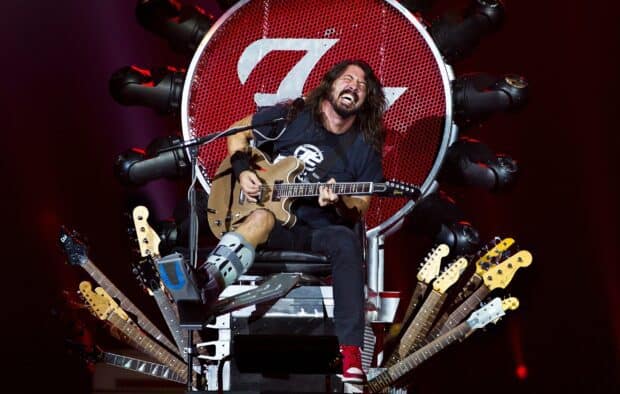 Dave Grohl is performing live with his guitar while sitting on a throne surrounded by multiple guitars, 2K Desktop Wallpaper