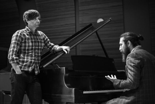Two musicians are discussing music beside a grand piano in a studio, HD Desktop Wallpaper