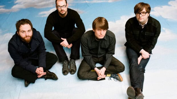 The band Death Cab For Cutie sits on a blue surface with a cloudy sky backdrop, HD Desktop Wallpaper