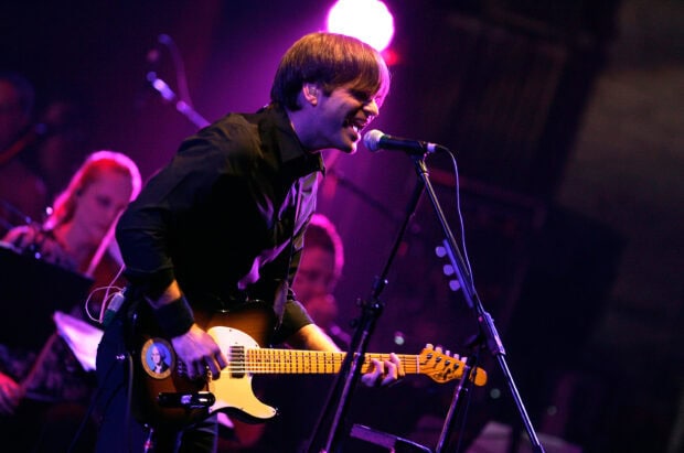 The musician is singing while playing guitar on stage with purple lighting, 2K Desktop Wallpaper