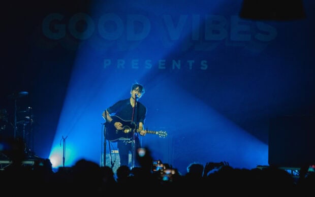 A musician from Death Cab For Cutie plays guitar and sings on stage with blue lighting, 2K Desktop Wallpaper