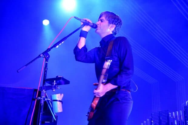 A band member is intensely singing and playing guitar on stage, 2K Desktop Wallpaper