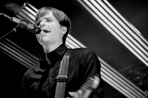 A close up of a band member singing passionately with guitar during a concert, 2K Desktop Wallpaper