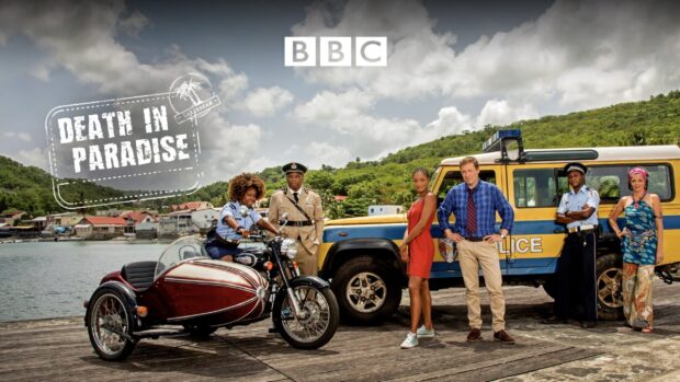 The main cast of Death In Paradise TV series stand near a police vehicle and motorcycle on a dock by the sea, 2K Desktop Wallpaper