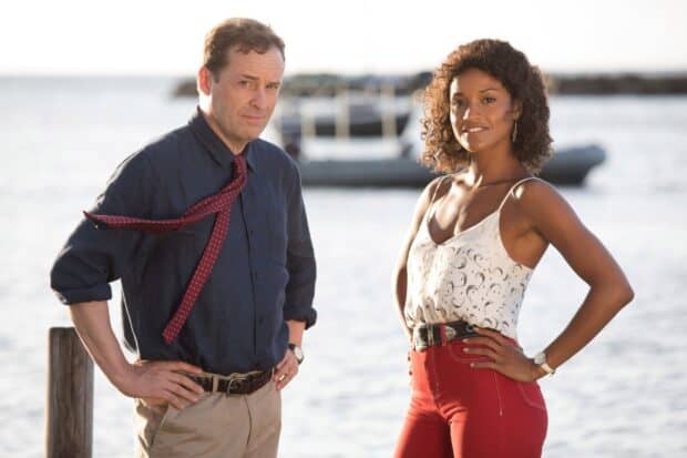 Two main characters from Death In Paradise tv series pose near the water with a boat in the background, HD Desktop Wallpaper