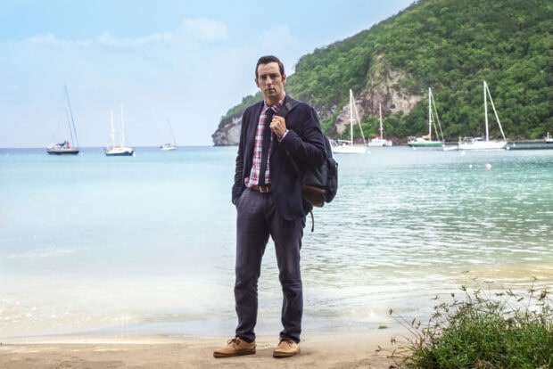 A man stands on a beach with boats and a hill behind in Death In Paradise Tv Series Wallpapers, HD Desktop Wallpaper