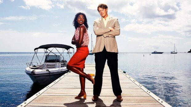 Two main characters from Death In Paradise stand on a pier near the ocean with boats in the background, HD Desktop Wallpaper