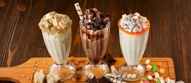 Three milkshake varieties with different toppings on a wooden board, 2K Desktop Wallpaper