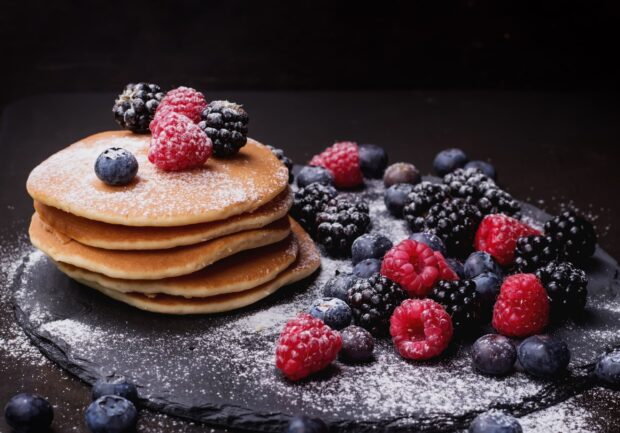 A stack of pancakes topped with fresh raspberries and blackberries on a dark slate plate, 2K Desktop Wallpaper
