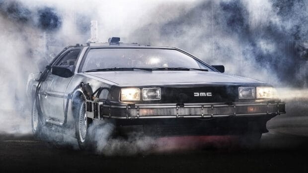 A Delorean Dmc 12 car is surrounded by smoke with its headlights on in a dramatic setting, 4K Desktop Wallpaper