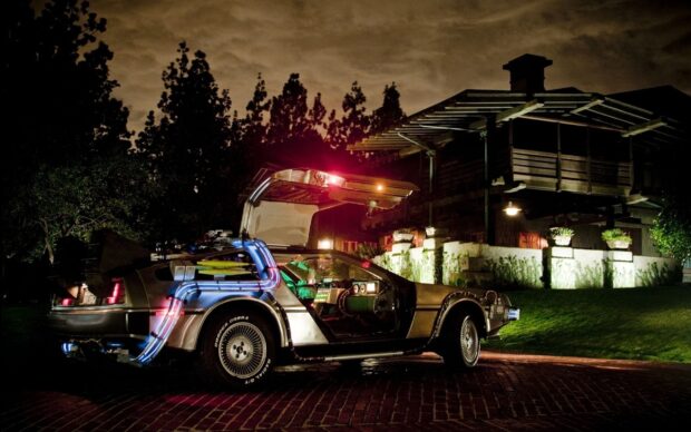 A Delorean Dmc 12 is parked outside a house at night with its gullwing door open and glowing tubes, 2K Desktop Wallpaper