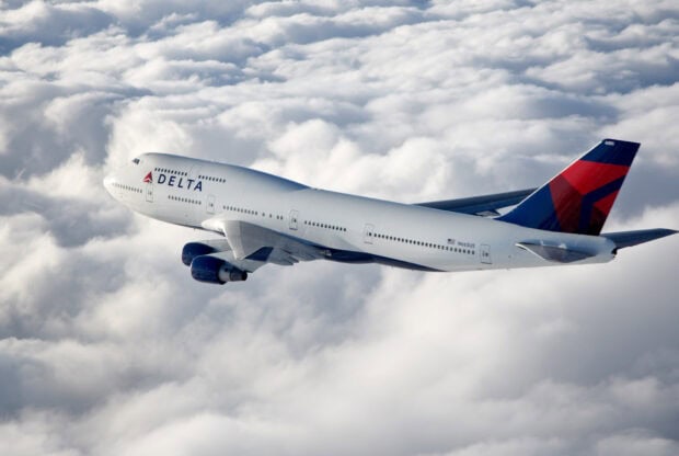 A Delta Air Lines airplane is captured flying high above the clouds on a clear day, HD Desktop Wallpaper