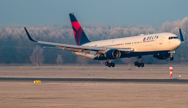 A Delta Air Lines airplane is landing on the runway with trees in the background, HD Desktop Wallpaper
