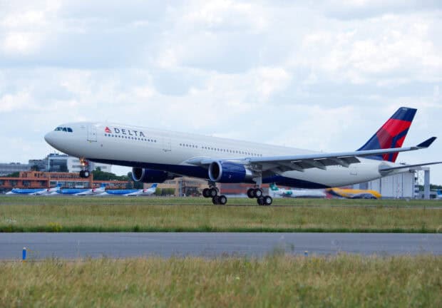 A Delta Air Lines airplane is landing on the runway with airport buildings in the background, 2K Desktop Wallpaper