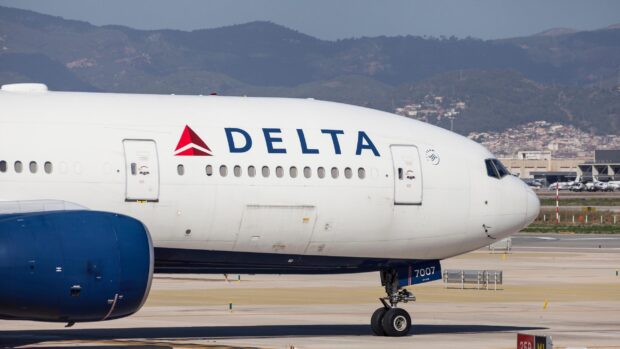 A Delta Air Lines plane is parked on the runway with mountains in the background, 2K Desktop Wallpaper