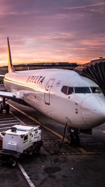 A Delta Air Lines plane is parked at the gate during sunset with a vivid sky in the background, HD Mobile Wallpaper