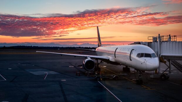 A Delta Air Lines plane is parked at the gate during a colorful sunset with dramatic clouds, HD Desktop Wallpaper