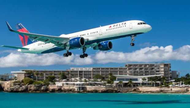 A Delta Air Lines aircraft is captured flying low over turquoise water near a coastal resort, HD Desktop Wallpaper