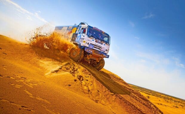 A rally raid truck speeds through desert sand kicking up dust, 2K Desktop Wallpaper