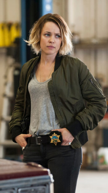 A detective from True Detective tv series stands with a serious expression and a badge on her belt, 2K Mobile Wallpaper