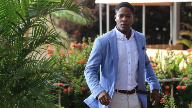 A man wears a blue jacket walking through a garden in Death In Paradise tv series wallpapers, HD Desktop Wallpaper