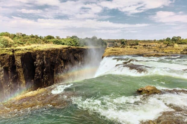 The Devils Pool at Victoria Falls in Zambia shows cascading water and a rainbow over rocky cliffs, 2K Desktop Wallpaper