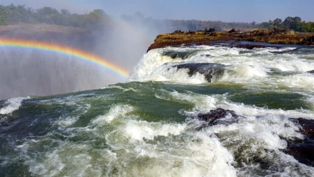 The Devils Pool in Zambia shows cascading water and a bright rainbow over the falls, HD Desktop Wallpaper