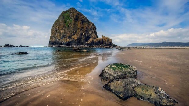 A large rocky formation rises from the shallow waters along the sandy coast under a cloudy sky in Dominica, 4K Desktop Wallpaper