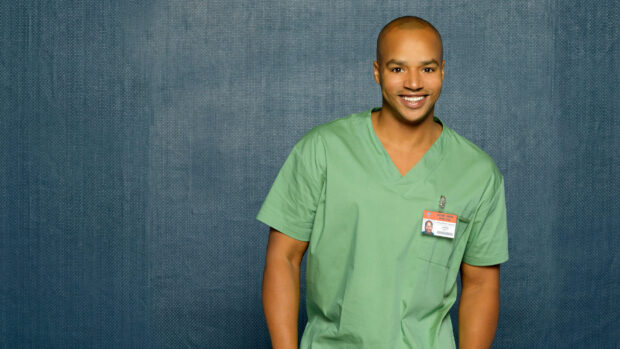 Donald Faison smiles wearing green medical scrubs against a blue backdrop, HD Desktop Wallpaper