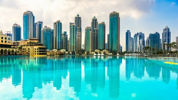 The Dubai skyline features modern architecture and turquoise water reflecting the buildings, 4K Desktop Wallpaper