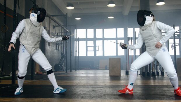 Two fencers are engaged in a duel inside a training hall wearing full fencing gear, 4K Desktop Wallpaper