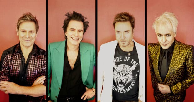 The Duran Duran members pose against a red wall wearing colorful jackets, 2K Desktop Wallpaper