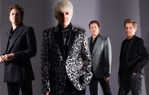 The Duran Duran band stands together in stylish patterned suits and jackets against a gray background, HD Desktop Wallpaper