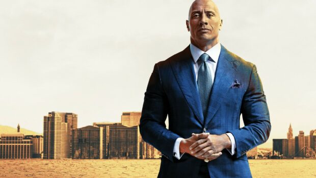 Dwayne Johnson stands confidently in a blue suit with a cityscape background, 2K Desktop Wallpaper