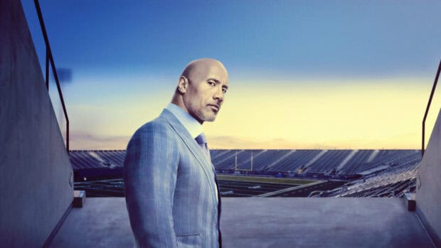 Dwayne Johnson stands confidently in a patterned suit with a stadium in the background, 4K Desktop Wallpaper
