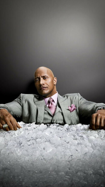 Dwayne Johnson is sitting confidently behind a pile of ice wearing a gray pinstripe suit, 2K Phone Wallpaper