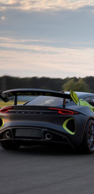 The Lotus Emira is captured speeding on a race track under cloudy skies, 2K Phone Wallpaper