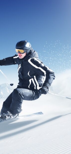 A skier wearing black gear is carving through fresh snow under a clear blue sky, HD Mobile Wallpaper