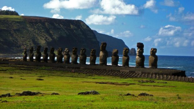 The Easter Island Moai statues stand in a row beside the ocean and green fields under a partly cloudy sky, HD Desktop Wallpaper