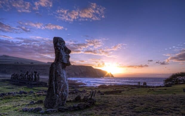 A large Easter Island statue faces the vibrant sunset near the ocean shore, 2K Desktop Wallpaper