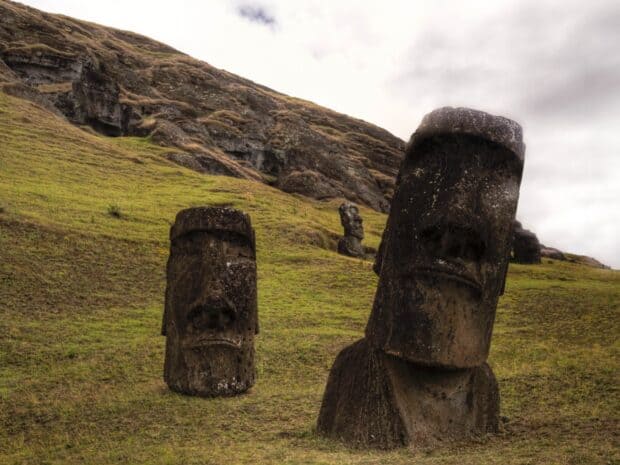 Two large stone heads from Easter Island stand on green hills with a cloudy sky, HD Desktop Wallpaper