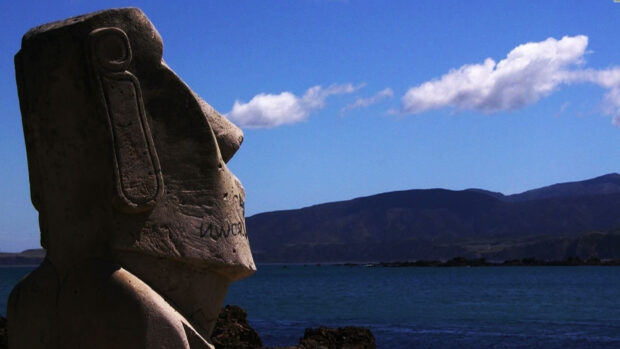 A large Easter Island statue overlooks the blue ocean and distant mountains under a clear sky, HD Desktop Wallpaper