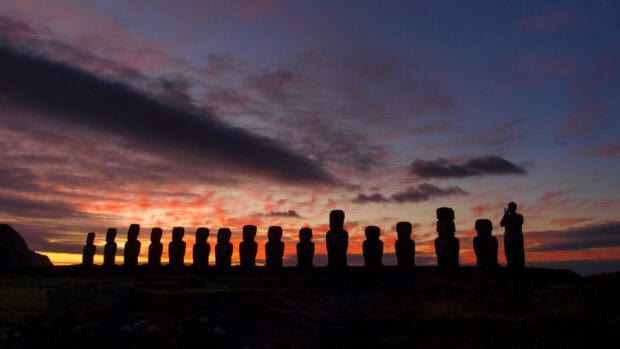 A person photographs Easter Island statues under a colorful sunset sky, HD Desktop Wallpaper