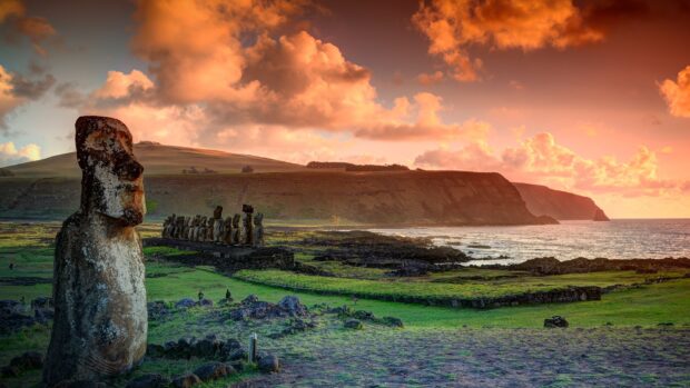 Easter Island statues stand against a vibrant sunset sky by the ocean, HD Desktop Wallpaper